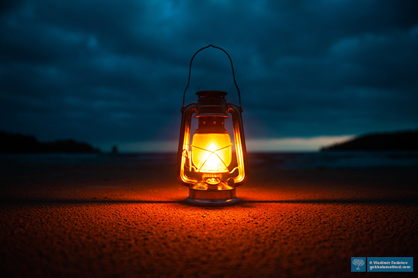 Photo of a kerosine lamp glowing against a darkened sky.