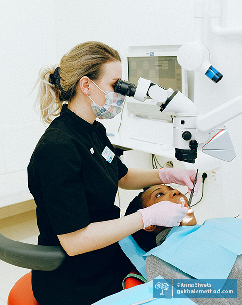 Dentist treating a patient, using a surgical telescope.