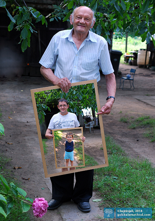 Photo of old man, holding photo of his son, holding photo of his grandson.