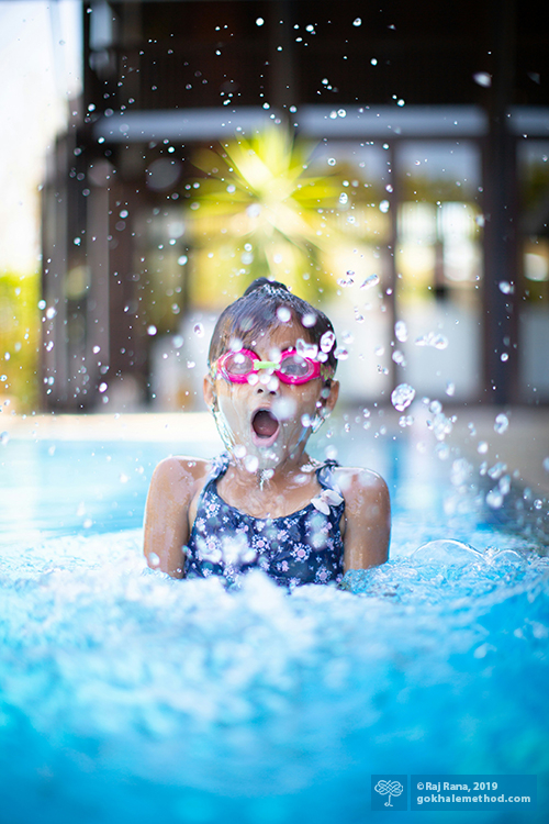 Young girl splashing/jumping in swimming pool.