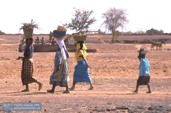 3 African women and girl walking in line headloading