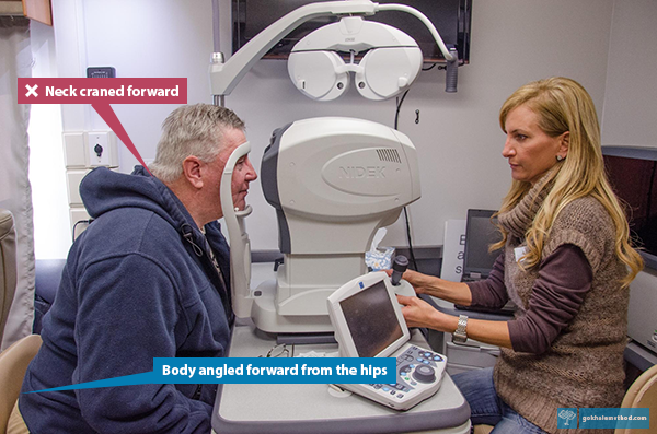 Man leaning in to rest his chin on a machine for eye examination by an optometrist.